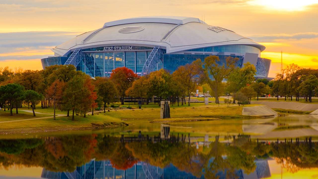 A football-shaped stadium next to fall trees and a body of water