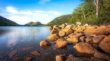 Rocks and water in the foreground with hills and trees at the back