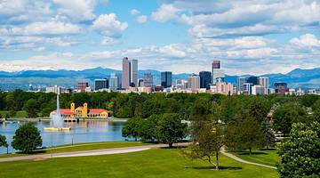 A park with green grass, trees, a lake, and a skyline in the background A park with green grass, trees, a lake, and a skyline in the background