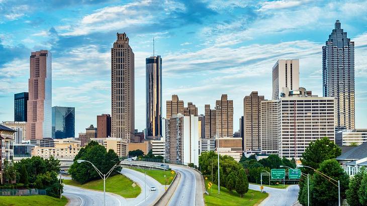 A skyline with tall buildings and a road, trees, and grass in the foreground