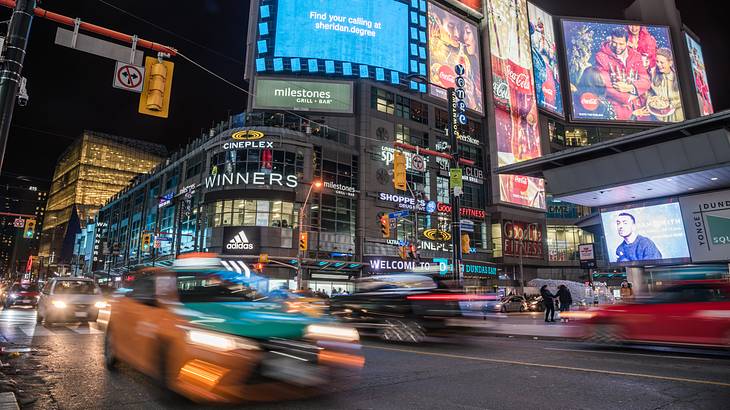 Large ad billboards on a busy street corner with blurred car lights