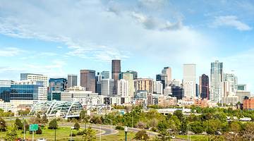 A skyline with buildings and a bridge and park in front of it under a blue sky