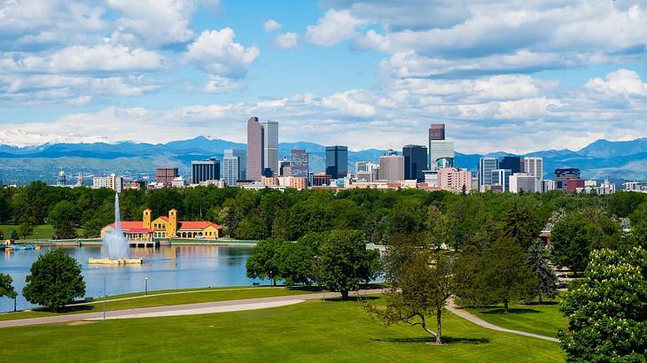 A park with green grass, trees, a lake, and a skyline in the background