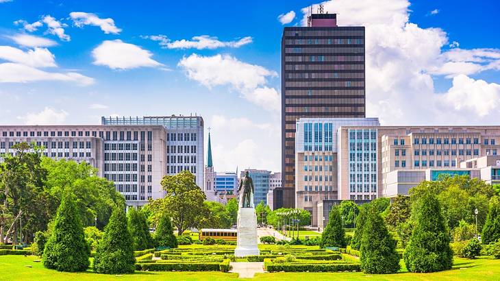 A statue surrounded by green grass and trees with a tall building behind it