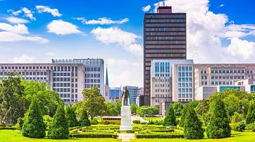 A statue surrounded by green grass and trees with a tall building behind it