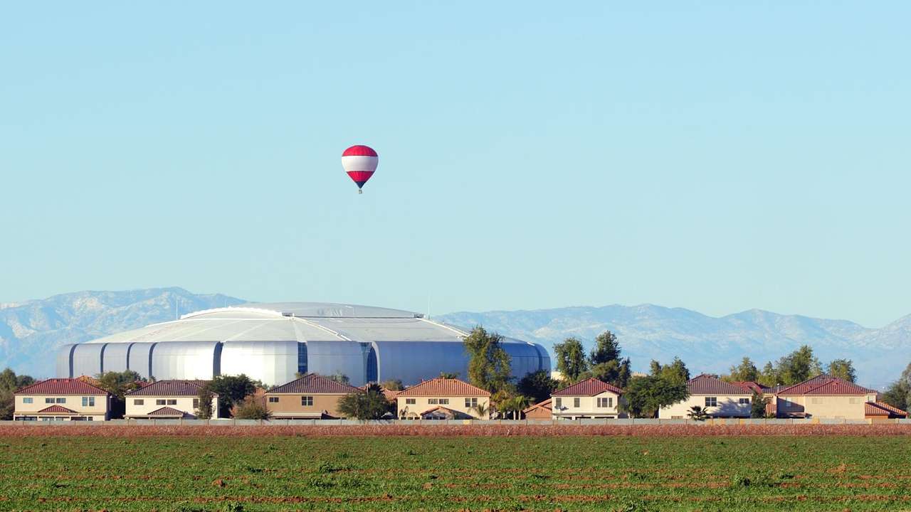 Houses, a round silver structure, and a field under a blue sky with a hot air balloon