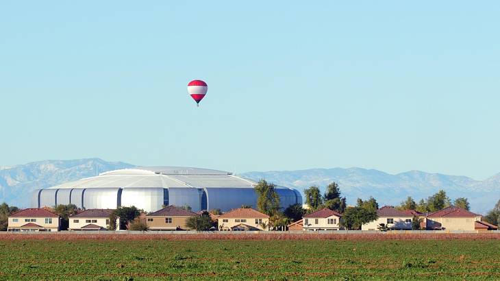 Houses, a round silver structure, and a field under a blue sky with a hot air balloon