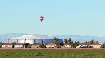 Houses, a round silver structure, and a field under a blue sky with a hot air balloon