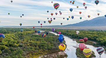 Air balloons in mid-air over a river surrounded by forests