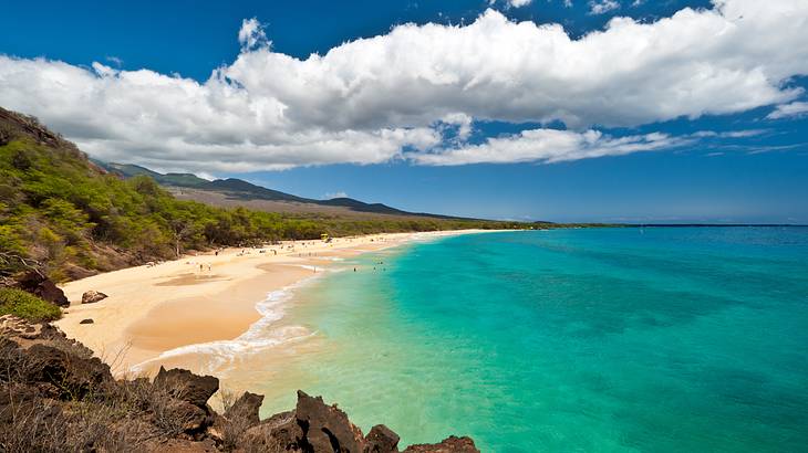 A beach with turquoise water, white sand, and mountainous scenery on a nice day