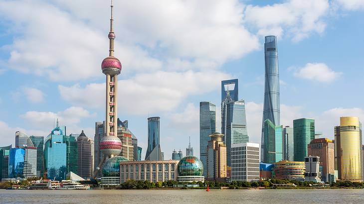 A city skyline is seen from across water, underneath a blue sky with fluffy clouds