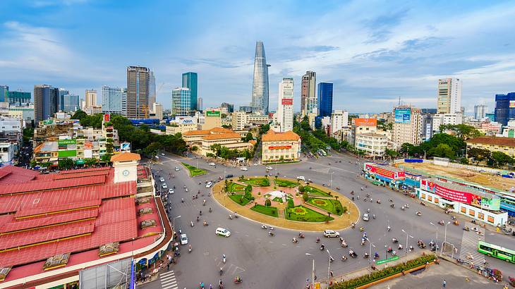 A road with vehicles and a roundabout surrounded by buildings, and a city skyline