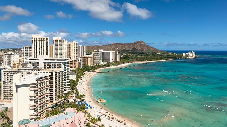 A beach with high-rise buildings to the left, a mountain, and a partly cloudy sky