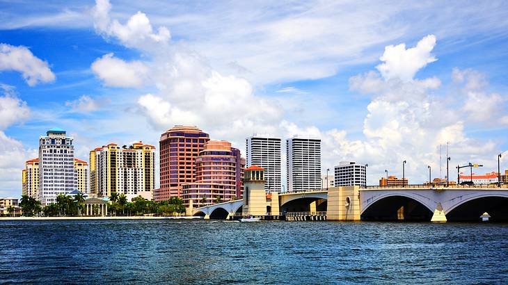 A cityscape with tall skyscrapers, a bridge, and a body of water in the foreground