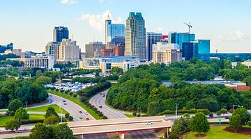 A city skyline next to a road and lots of green trees under a blue sky