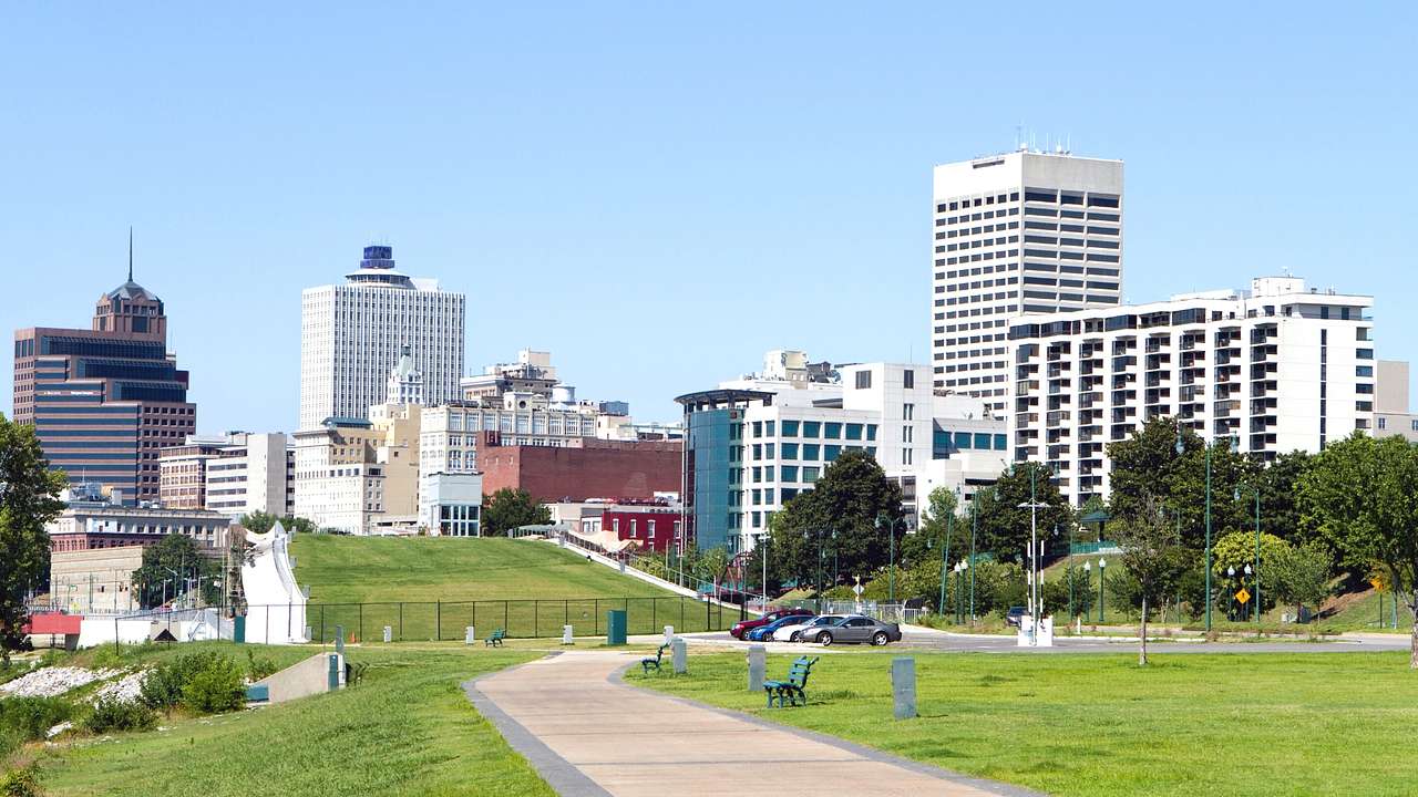 A park with a path through the grass next to city buildings on a clear day