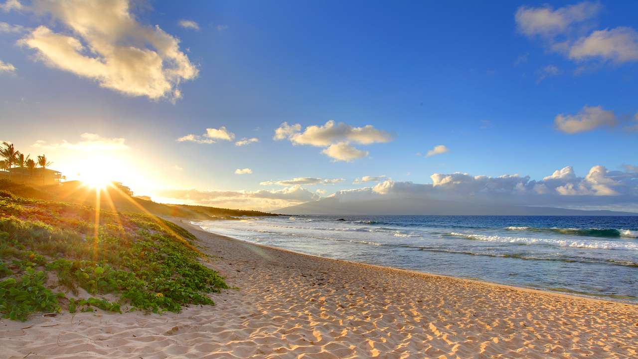 A white sandy beach with small waves coming to shore under the rising sun
