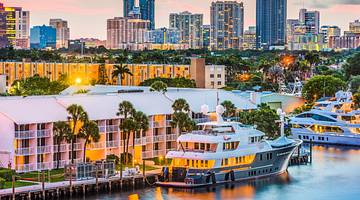A view of a waterfront at sunset with boats, illuminated buildings, and trees A view of a waterfront at sunset with boats, illuminated buildings, and trees