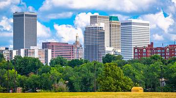 A city skyline next to green trees and grass under a blue sky with clouds