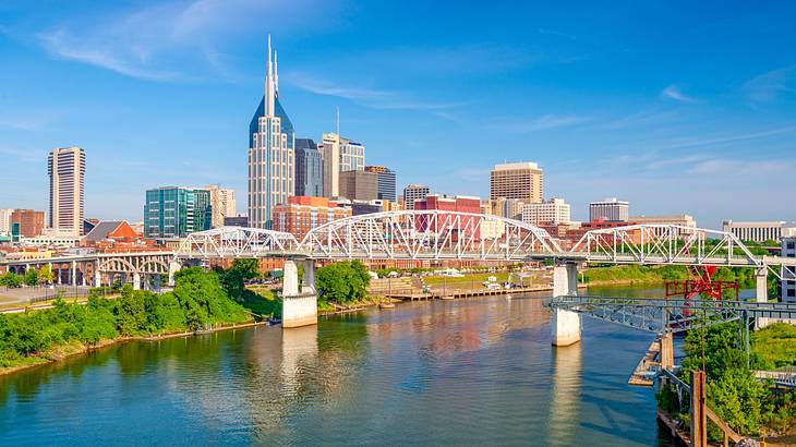 A city skyline next to a river with a bridge over it under a blue sky