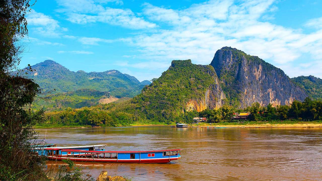 A river with a boat on it next to greenery-covered hills under a blue sky