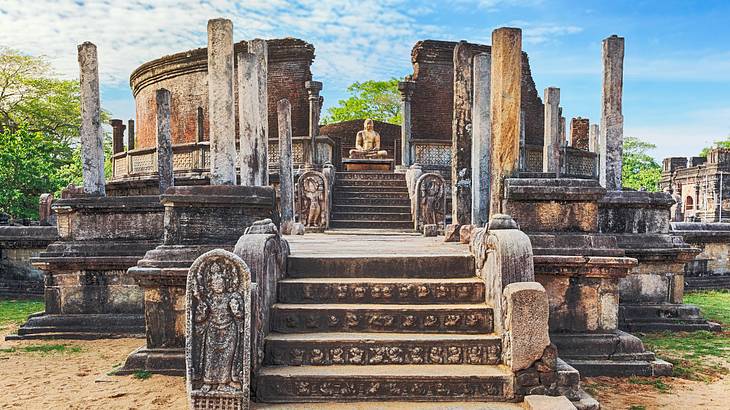 An ancient circular monument with pillars, steps, carvings, and an idol in the centre