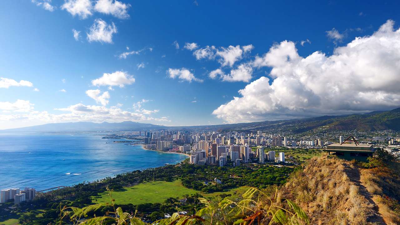 Aerial view of a city skyline, green mountains, the ocean, and a partly cloudy sky