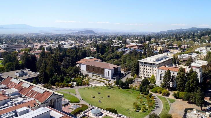 An aerial view of a city with buildings and greenery next to mountain ranges