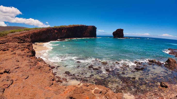 A body of water next to rocks and a cliff under a partly cloudy sky