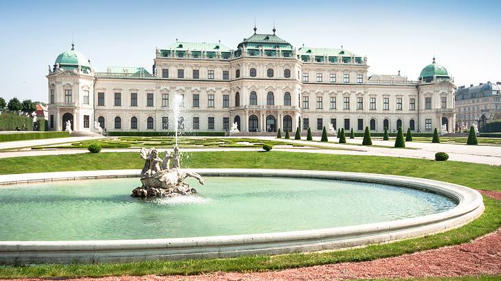 Looking towards a spurting fountain in front of a white grand palace on a nice day