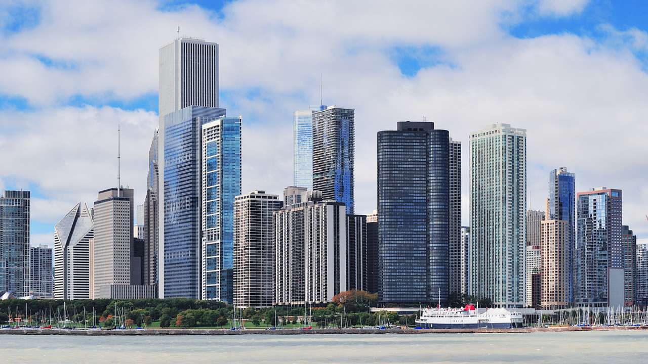 A city skyline full of tall modern glass buildings with a partly cloudy sky behind