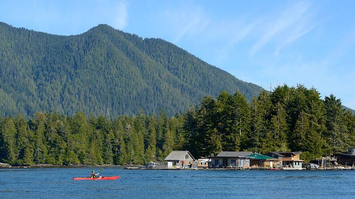 A body of water with a kayak on it next to a greenery-covered hill and small houses