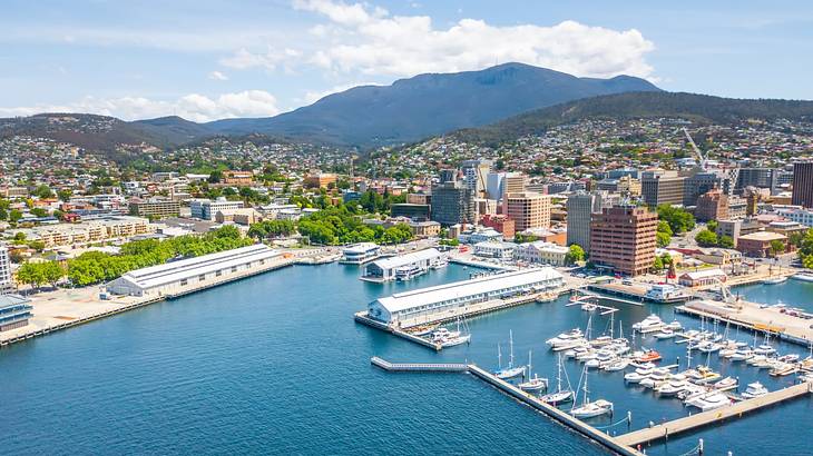 A blue harbor with boats surrounded by buildings and mountains under a blue sky