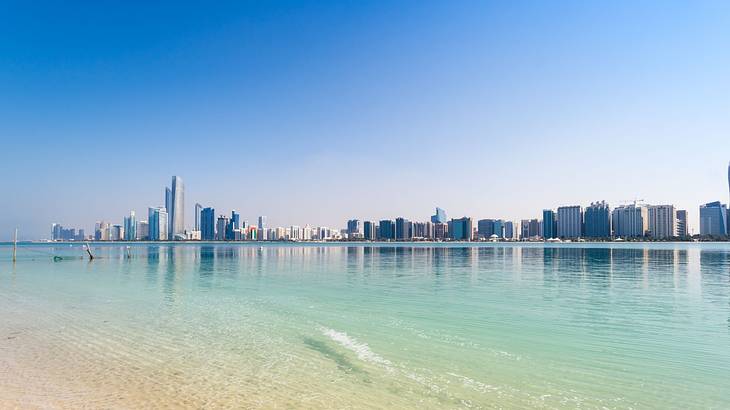 A white-sand beach and clear ocean with a distant view of skyscrapers