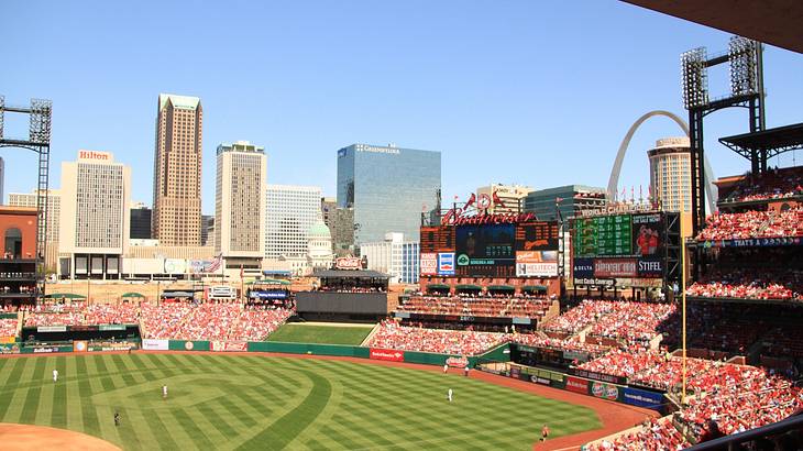 Buildings, an arch, blue sky, and a baseball stadium full of people