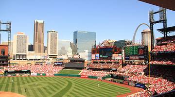 Buildings, an arch, blue sky, and a baseball stadium full of people