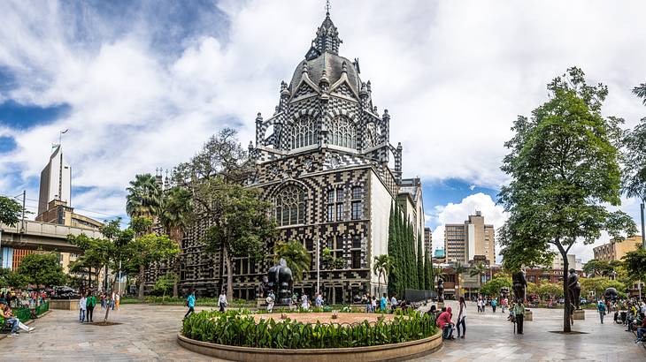 A square with greenery next to a black and white cathedral-style building