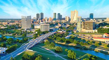 A view over a city with skyscrapers next to trees, a river, roads, and a bridge