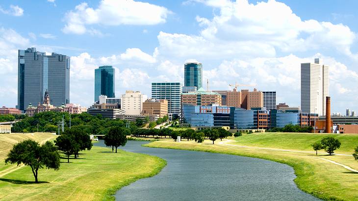 A body of water surrounded by lush grass and urban skyscrapers on a sunny day