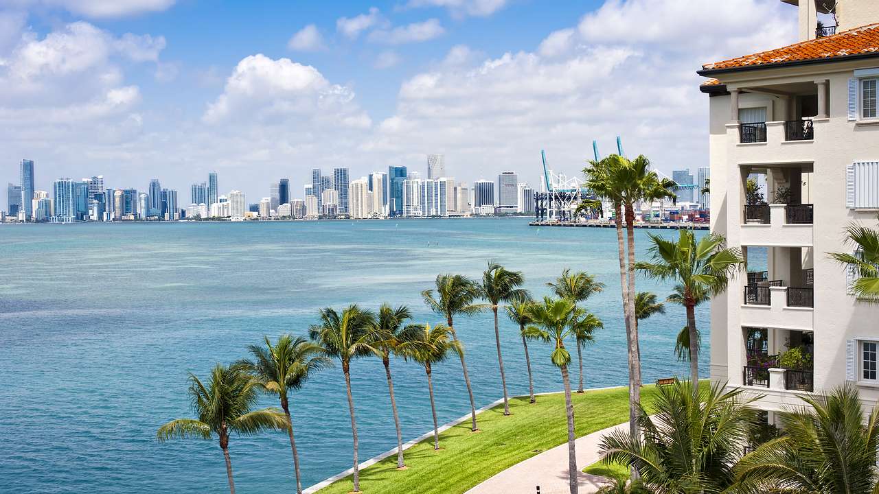 A building next to palm trees and the blue ocean with a skyline in the distance