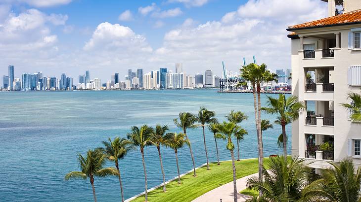 A building next to palm trees and the blue ocean with a skyline in the distance