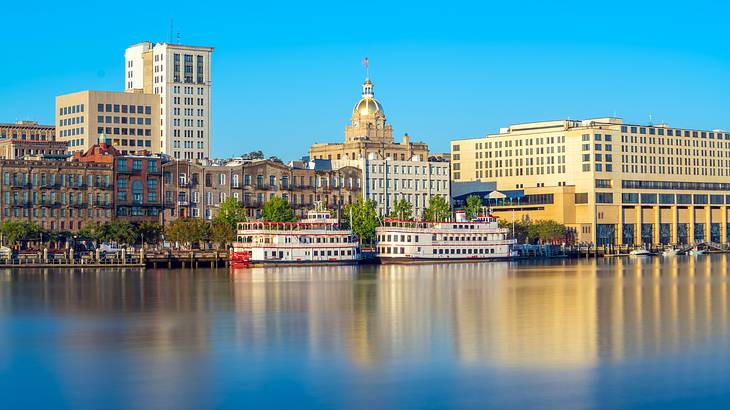 Two red and white riverboats on a body of water surrounded by buildings