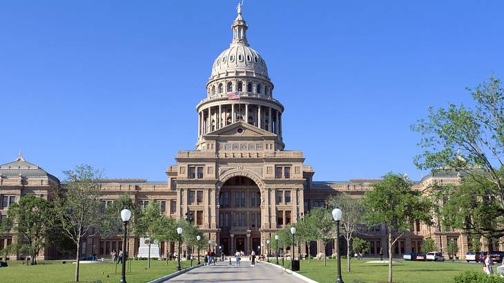 A large stone building with a dome next to a path, grass, and trees