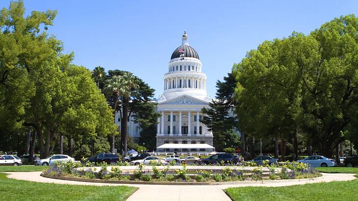 A large white stone state capitol building with a dome next to a garden