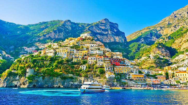 Colorful buildings on a hilly terrain near rocky mountains and the sea with a ship