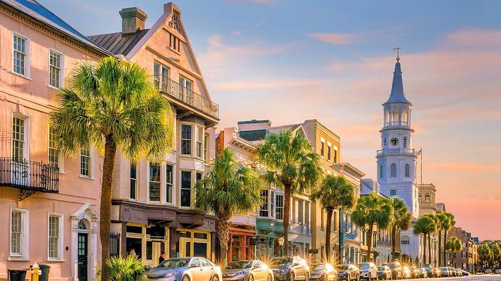 Colorful buildings, a white tower, and parked cars on a palmed-lined street