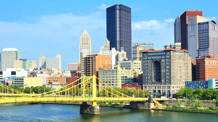 A yellow bridge across a river with tall buildings on the shore