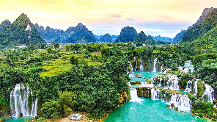 Multiple waterfalls falling off a luscious green cliff into the water below