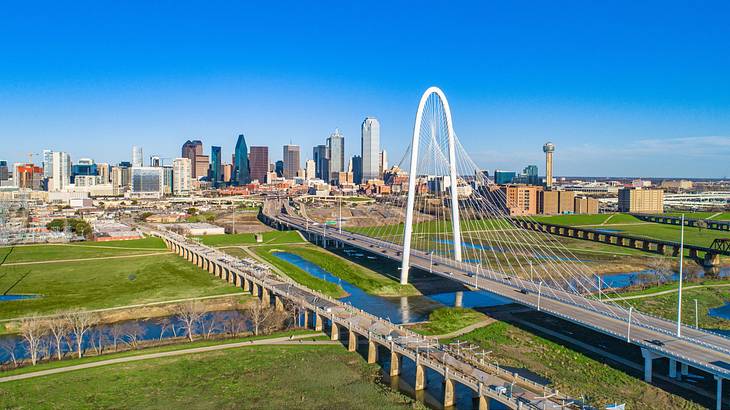 A view over a city next to grass and a bridge over water under a blue sky