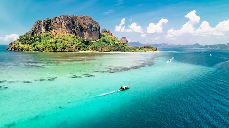 A mountainous island and moving boats next to the turquoise ocean